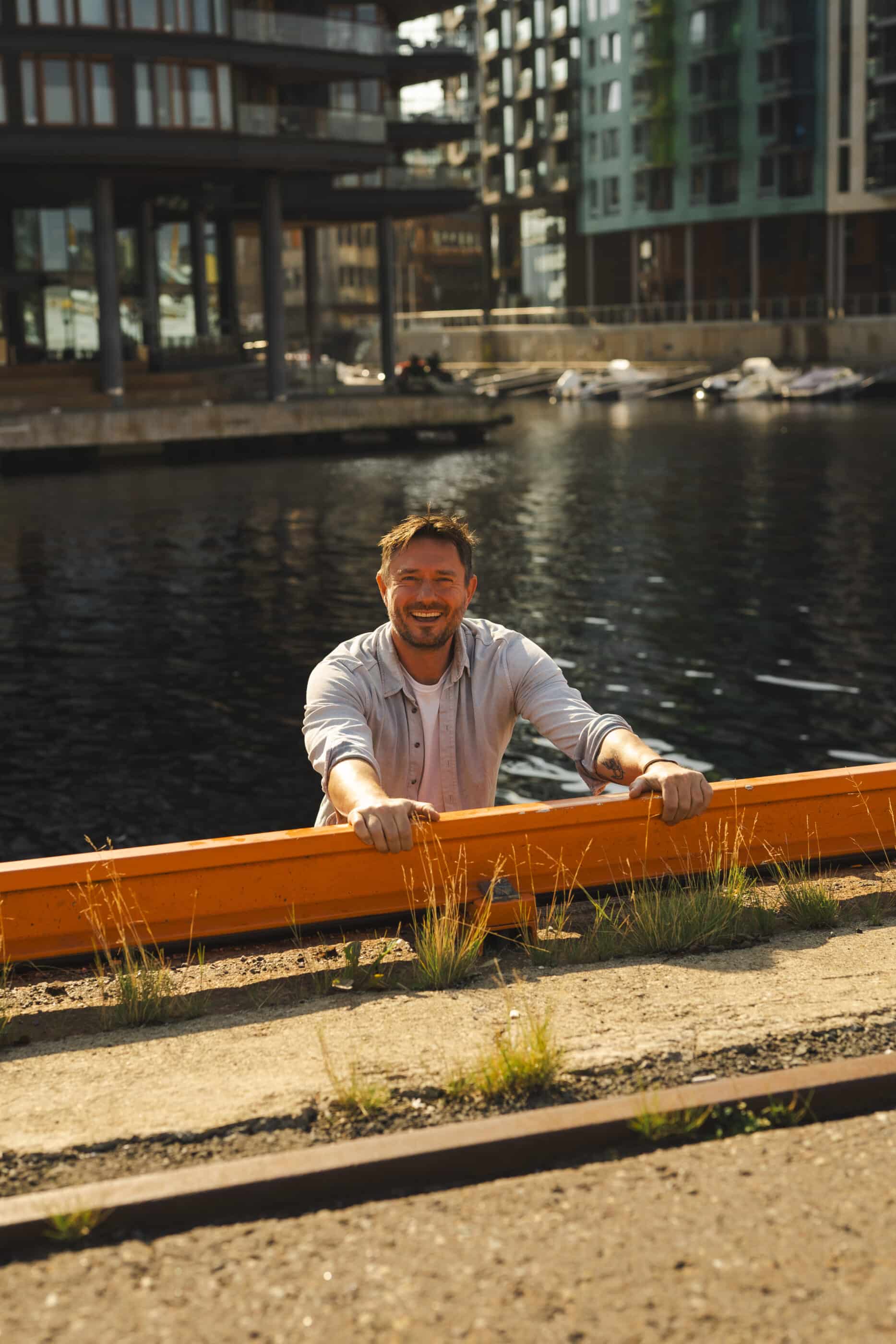 A smiling man leans on an orange railing by a waterfront with modern buildings behind him, accompanying a positive review of corporate emcees Mo and Katy.